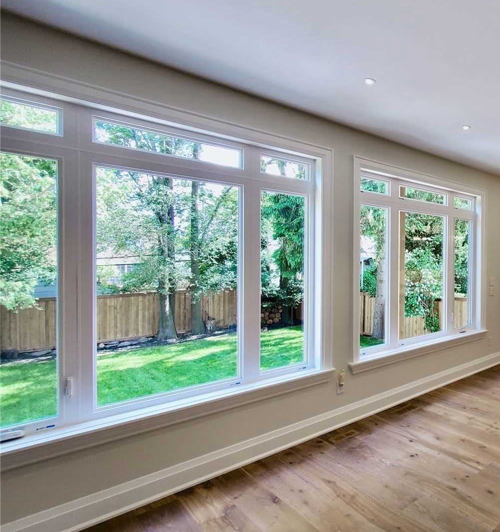 Large white-framed living room windows overlooking a backyard