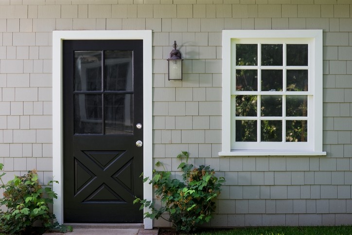 Installed black entry door and white window with grills enhancing an Abbotsford home’s exterior
